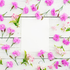 Floral pattern of pink flowers and paper card on white rustic background. Flat lay, top view. Floral concept