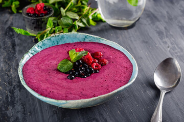 Ceramic bowl with berry smoothie decorated with currant, raspberry and mint on the black wooden background - Well being, Healthy eating, Detox or Diet concept. Selective focus