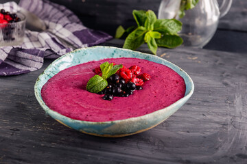 Ceramic bowl with berry smoothie decorated with currant, raspberry and mint on the black wooden background - Well being, Healthy eating, Detox or Diet concept. Selective focus