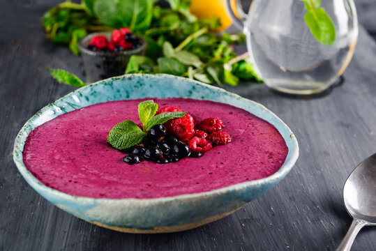 Ceramic bowl with berry smoothie decorated with currant, raspberry and mint on the black wooden background - Well being, Healthy eating, Detox or Diet concept. Selective focus