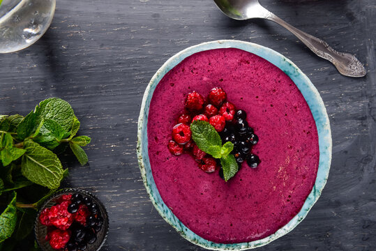Top view Ceramic bowl with berry smoothie decorated with currant, raspberry and mint on the black wooden background - Well being, Healthy eating, Detox or Diet concept. Selective focus