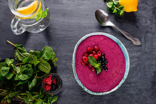Top view Ceramic bowl with berry smoothie decorated with currant, raspberry and mint on the black wooden background - Well being, Healthy eating, Detox or Diet concept. Selective focus