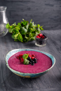 Ceramic bowl with berry smoothie decorated with currant, raspberry and mint on the black wooden background - Well being, Healthy eating, Detox or Diet concept. Selective focus