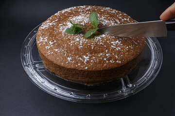 Woman cutting a chocolate cake with sugar decoration with a knife on glass stand

