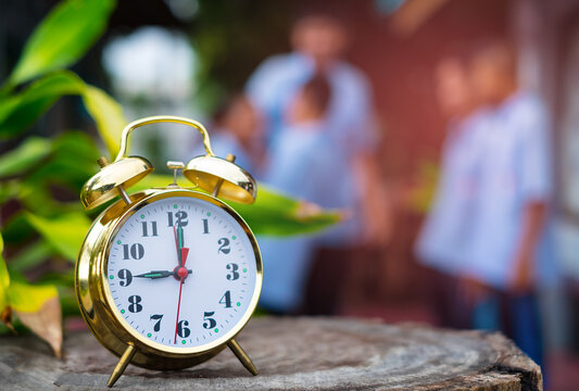 A golden alarm clock at 9 o'clock with Group of boys standing discussing in garden. Start up working concept in the morning. Close-up and blur background.