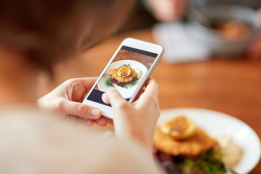 woman with smartphone photographing food at cafe