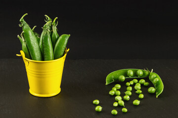 Green peas on a black background in a yellow decorative bucket Сору spase