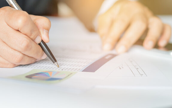 Hand holding pen for analyzing financial data and counting on document chart, business concept.
