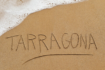 word Tarragona written in the sand of a beach