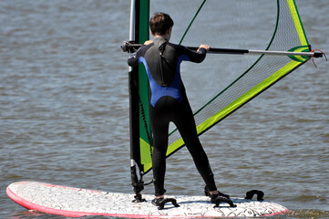 Ein Windsurfer stehend auf dem Surfboard hält das Segel, dabei gleitet er auf dem Wasser