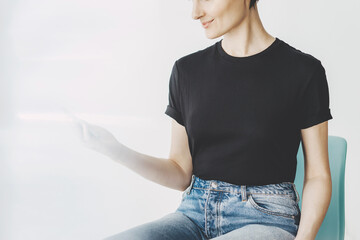 Close-up of young woman wearing black blank t-shirt and using modern smartphone, mock-up of black t-shirt, white wall on the background