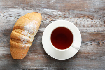 Fresh croissant with cup of tea on grey wooden table