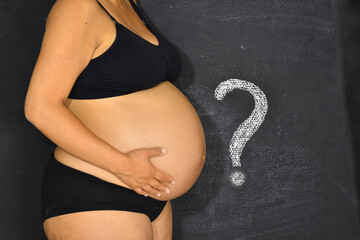 A pregnant woman standing next to a question mark.