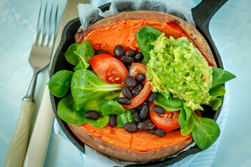 Baked whole sweet potato with guacamole and black beans in a cast-iron frying pan. Love for a healthy vegan food concept