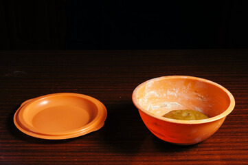 An orange cup with a dough stands alone on a wooden table on a black background.
