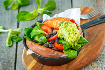 Baked whole sweet potato with guacamole and black beans in a cast-iron frying pan. Love for a healthy vegan food concept