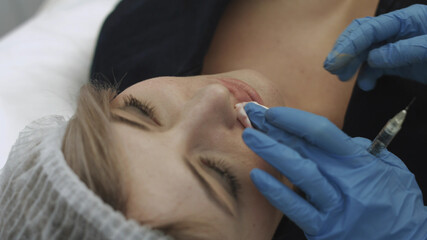 Beautician removes blood from the patient's mouth during the procedure of the lips augmentation