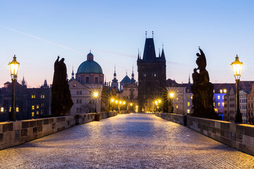 Fototapeta premium Praga, Republika Czeska. Most Karola ze statuetką i wschodem słońca nad mostem, w tle Wieża Mostu Staromiejskiego.