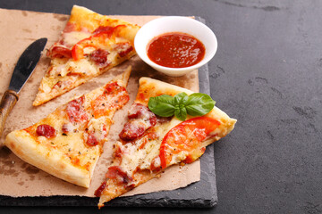 Pizza with sausage, ham, tomato and cheese, decorated with basil and cut into pieces on a parchment