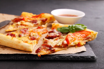 Pizza with sausage, ham, tomato and cheese, decorated with basil and cut into pieces on a parchment