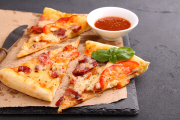 Pizza with sausage, ham, tomato and cheese, decorated with basil and cut into pieces on a parchment