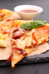 Pizza with sausage, ham, tomato and cheese, decorated with basil and cut into pieces on a parchment