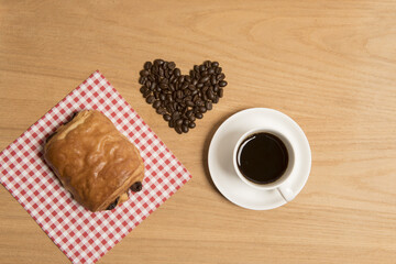 Black coffee in a cup and saucer with a croissant and coffee beans