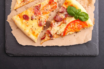 Pizza with sausage, ham, tomato and cheese, decorated with basil and cut into pieces on a parchment