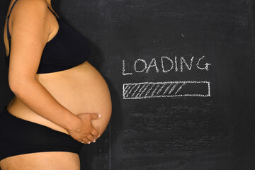 A pregnant woman standing next to a board with a loading sign drawn onto it.