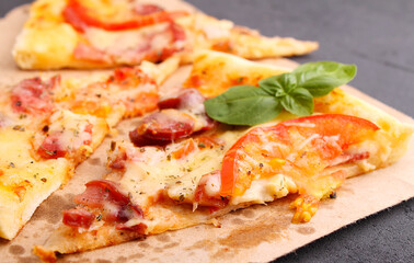 Pizza with sausage, ham, tomato and cheese, decorated with basil and cut into pieces on a parchment