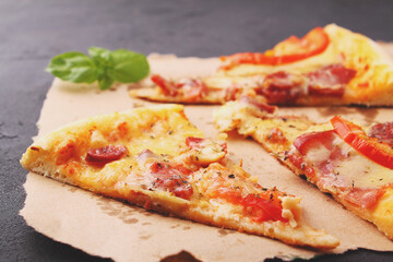 Pizza with sausage, ham, tomato and cheese, decorated with basil and cut into pieces on a parchment
