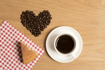 Black coffee in a cup and saucer with a piece of cake and coffee beans