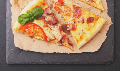 Pizza with sausage, ham, tomato and cheese, decorated with basil and cut into pieces on a parchment