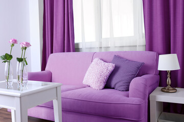 Sofa with beautiful pillows and focused vase with flowers on the table in front of it in the room