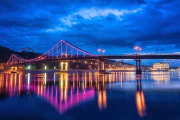 Deurstickers Night european city in colorful lights and reflection in water, Kyiv (Kiev) the capital of Ukraine. Pedestrian bridge across the Dnieper river and view to the river station © larauhryn