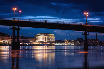 Fototapeta na wymiar Night european city in colorful lights and reflection in water, Kyiv (Kiev) the capital of Ukraine. Pedestrian bridge across the Dnieper river and view to the river station