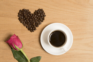 Black coffee in a cup and saucer with a red rose and coffee beans 