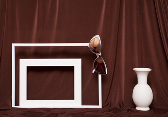 Two empty picture frames, glasses and vase on background of brown cloth.