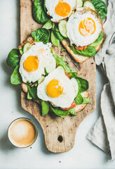 Healthy breakfast sandwiches and cup of coffee. Bread toasts with fried eggs and fresh vegetables on rustic wooden board over grey marble background, top view. Clean eating, healthy, diet food concept
