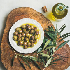Pickled green Mediterranean olives and olive tree branch on wooden board and virgin olive oil in...
