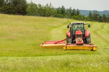 Work on an agricultural farm. A red tractor cuts a meadow.
