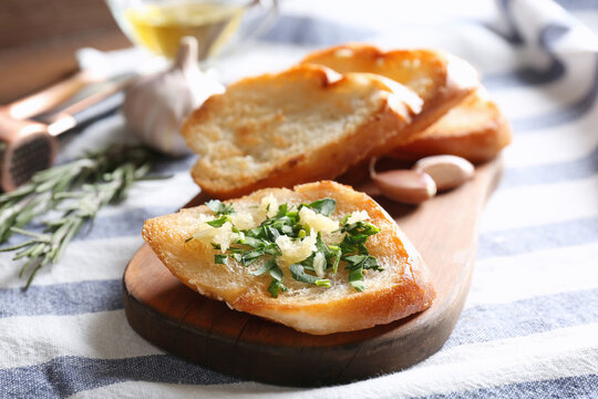 Tasty bread slices with garlic and herbs on wooden cutting board
