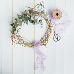 Eucalyptus and ivy wreath, scissors and sequin ribbon on white wooden background