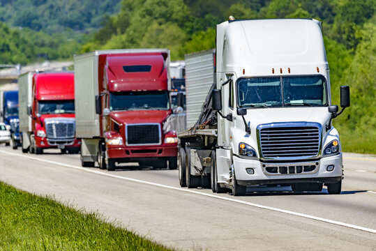 A solid line of eighteen-wheelers barrel down an interstate highway in Tennessee.  Heat waves rising from the pavement give a nice shimmering effect to vehicles and trees behind the lead truck.
