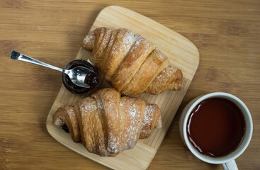 Delicious fresh croissants with fruit jam and tea on wooden