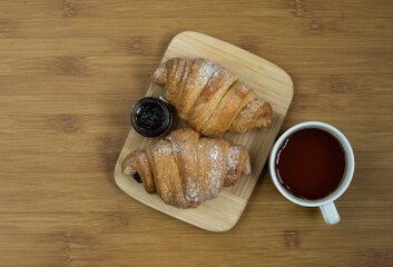 Delicious fresh croissants with fruit jam and tea on wooden