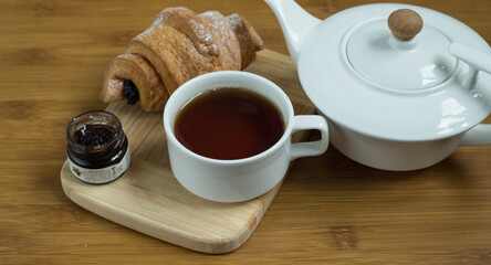Delicious fresh croissants with fruit jam and tea on wooden