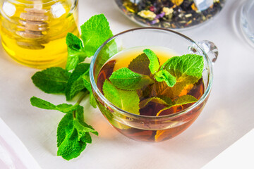 Mint tea in a cup, a jar of honey, a cookie in a jar, on a white tray in bed.