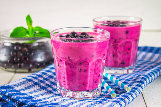 Smoothies of black currant in glass glasses with straws on a white wooden table.