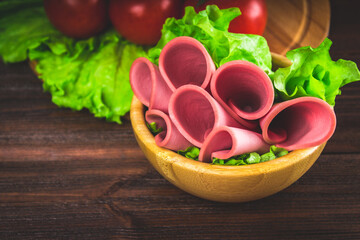 Sliced sausage with lettuce in a wooden plate. Gray background.